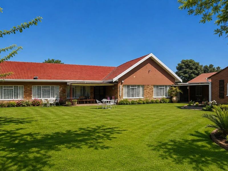 A well-maintained single-story brick house featuring a red tile roof, a spacious manicured lawn, and a covered rear patio area.