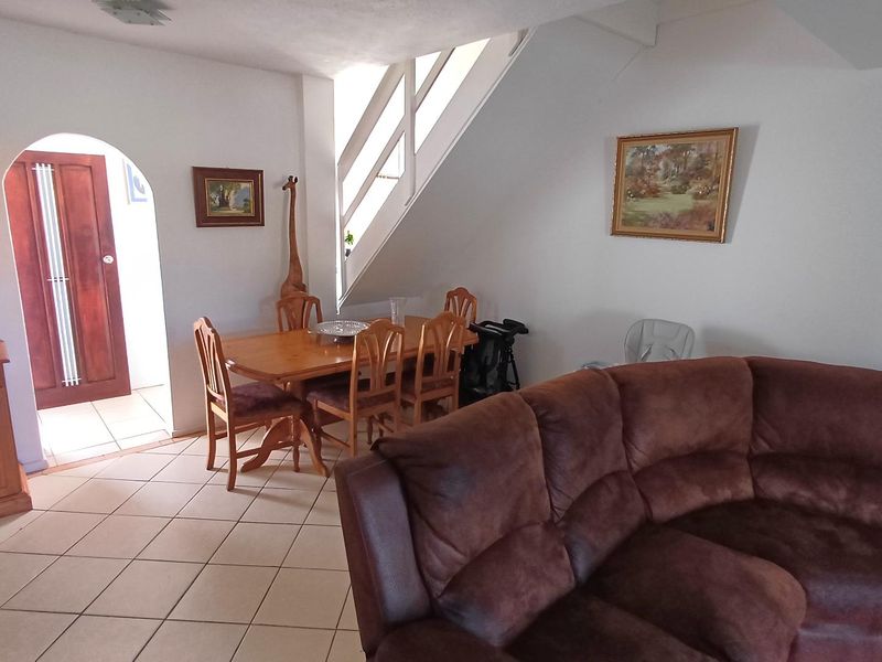 Open plan living and dining area featuring tiled flooring, an arched doorway, and a staircase with a wooden balustrade.