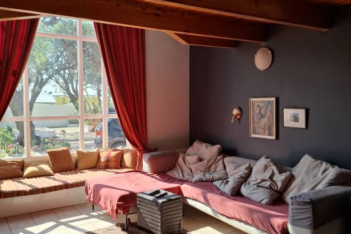 A bright living area featuring exposed timber ceiling beams, large floor-to-ceiling windows, and tiled flooring, offering a warm and inviting atmosphere.