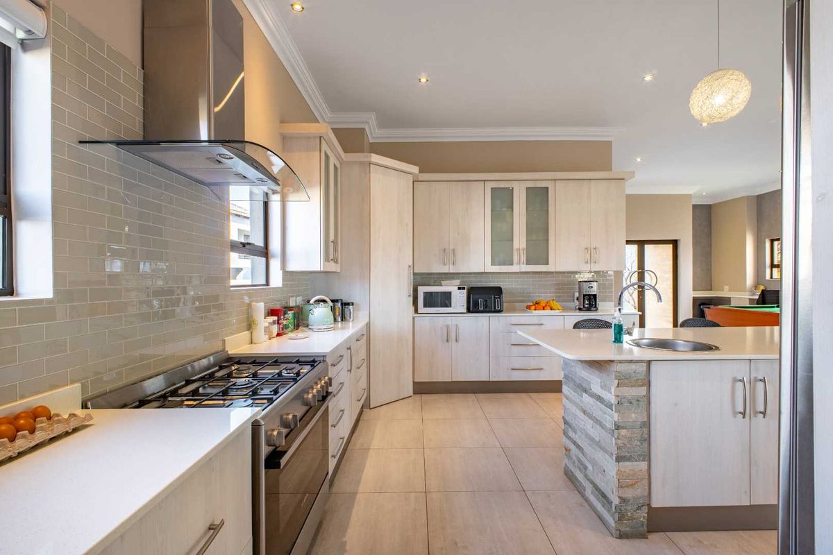 Modern kitchen featuring light wood cabinetry, stone-clad island, gas stove with extractor fan, and subway tile backsplash.