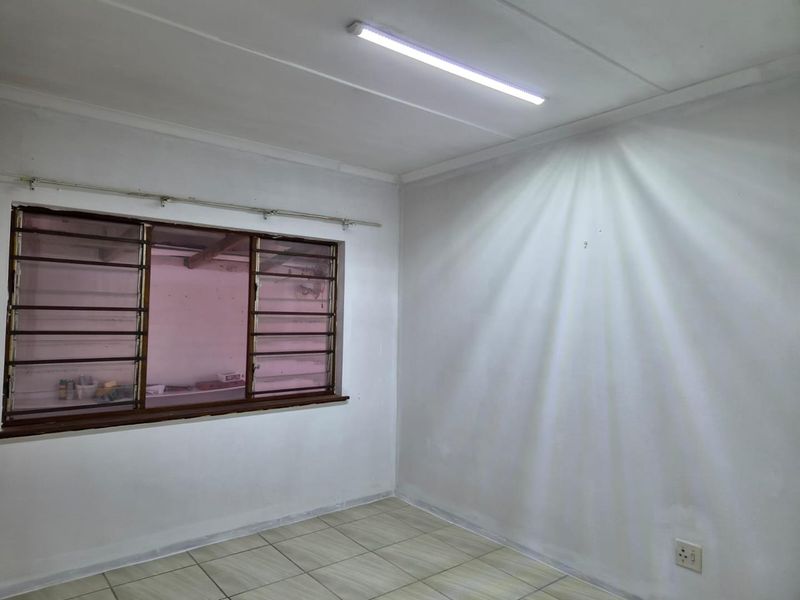 An empty bedroom featuring tiled flooring, a window with security burglar bars, and a basic fluorescent light fixture.