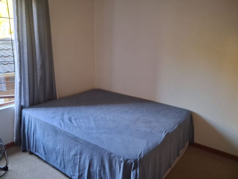 A simple bedroom featuring carpeted flooring and a window with security bars, providing a functional and neutral space.