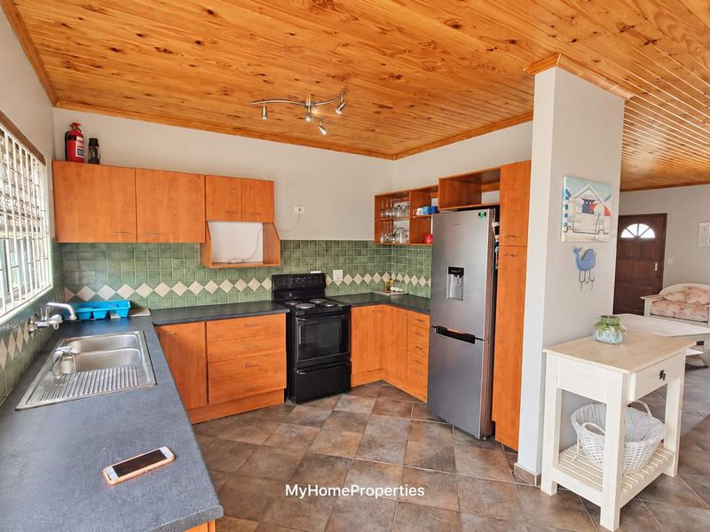 Open-plan kitchen featuring wooden ceilings, tiled flooring, and laminate cabinetry, seamlessly flowing into the adjacent living area.