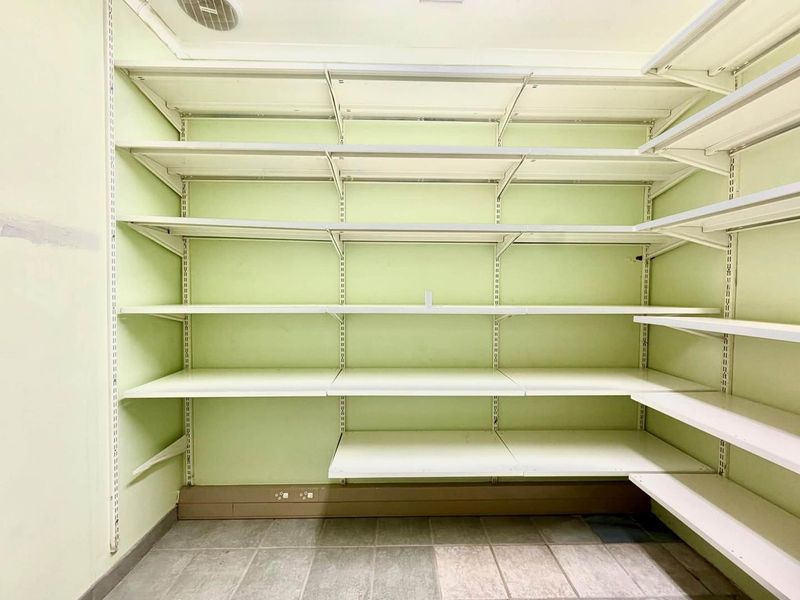 A functional utility or storage room featuring extensive wall-mounted shelving, tiled flooring, and integrated electrical points.