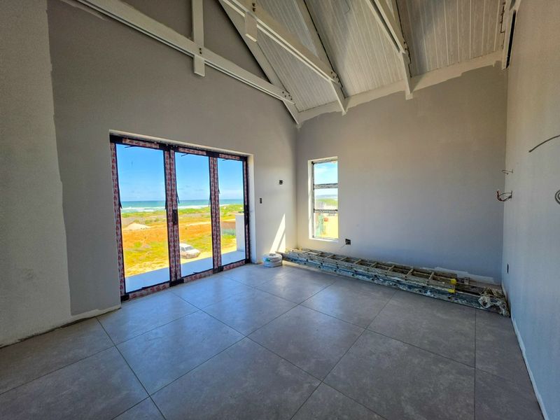 Spacious living area featuring vaulted ceilings with exposed trusses, large stacker doors opening to coastal views, and modern floor tiling, currently in finishing stages.