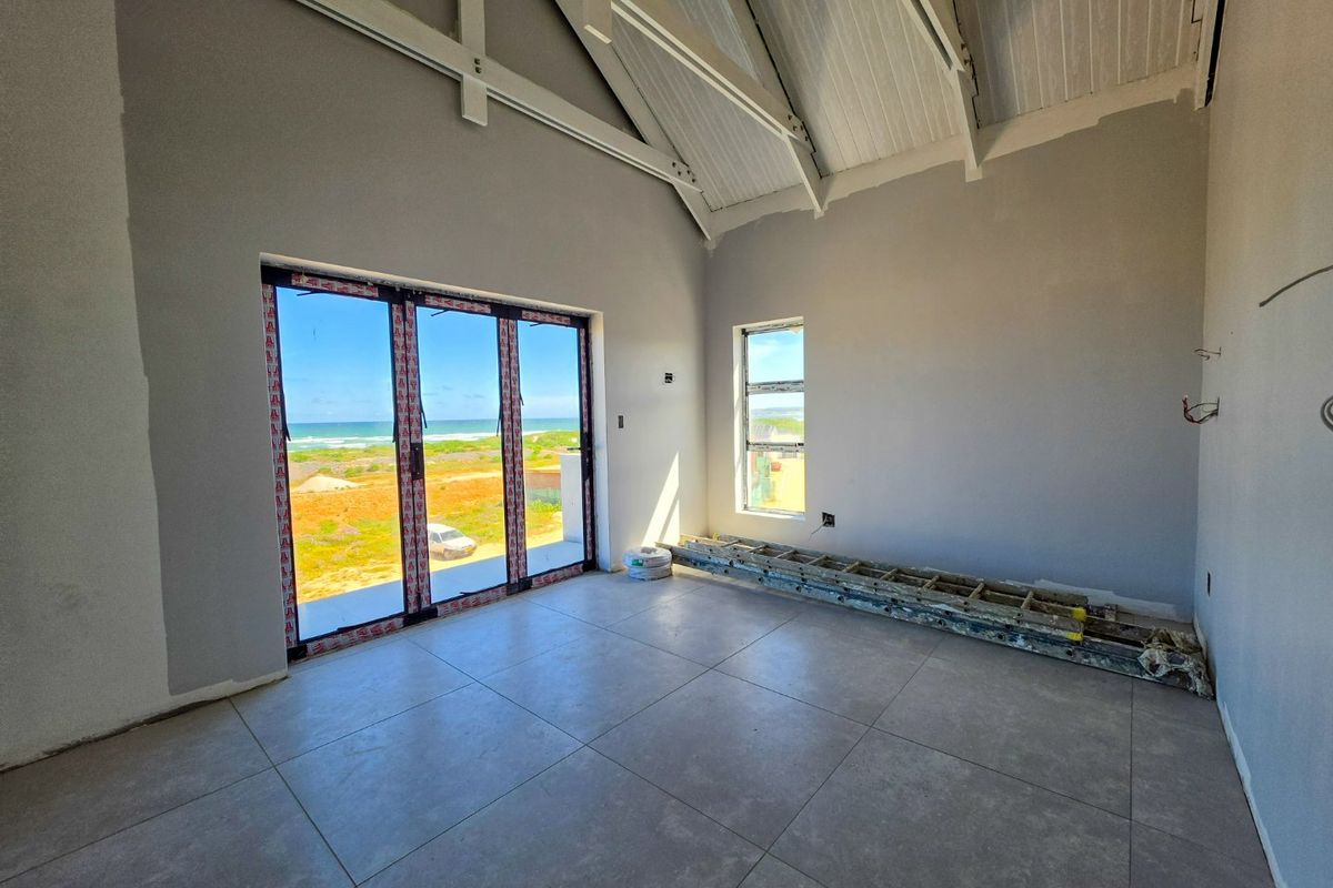Spacious living area featuring vaulted ceilings with exposed trusses, large stacker doors opening to coastal views, and modern floor tiling, currently in finishing stages.