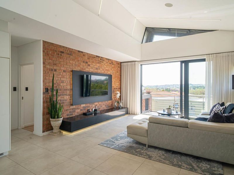Modern living room featuring an exposed brick feature wall, high raked ceilings, tiled floors, and large sliding doors opening to a balcony.
