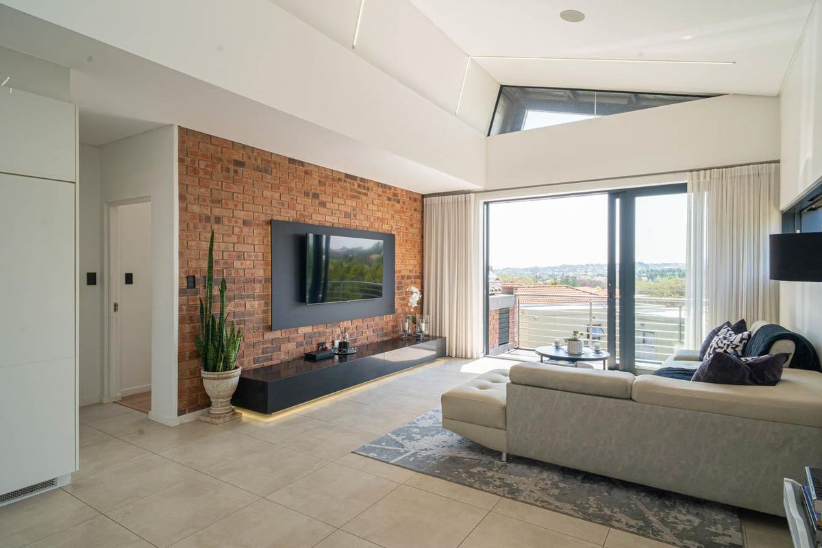 Modern living room featuring an exposed brick feature wall, high raked ceilings, tiled floors, and large sliding doors opening to a balcony.