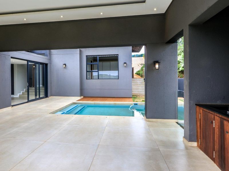 Spacious covered patio featuring a built-in braai, outdoor cabinetry, and direct access to a private swimming pool.
