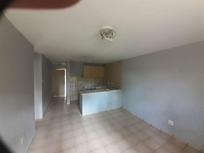 An open-plan living and kitchen area featuring tiled flooring, a breakfast counter, and built-in kitchen cabinetry with a hob and sink.