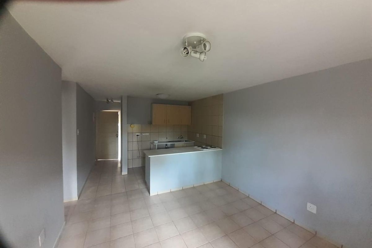 An open-plan living and kitchen area featuring tiled flooring, a breakfast counter, and built-in kitchen cabinetry with a hob and sink.