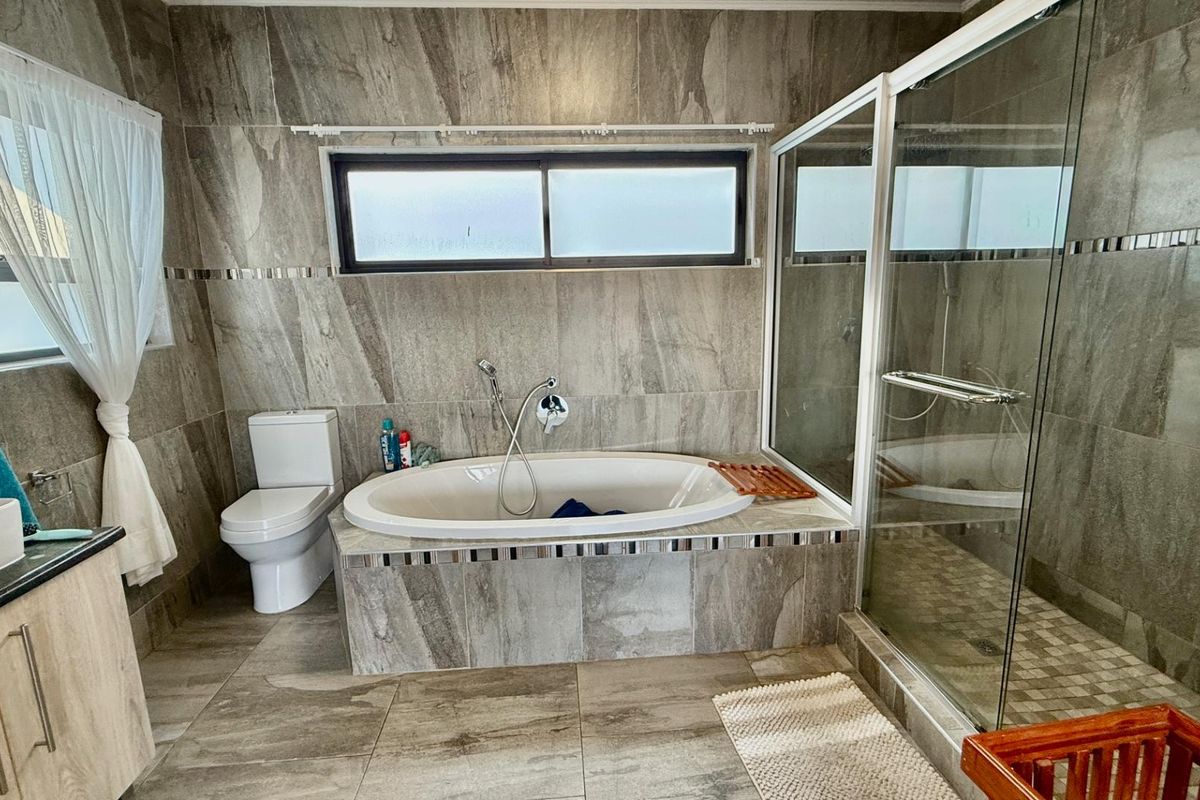 Modern bathroom featuring floor-to-ceiling stone-look tiling, a built-in oval bathtub, a separate glass-enclosed shower, and a vanity unit.