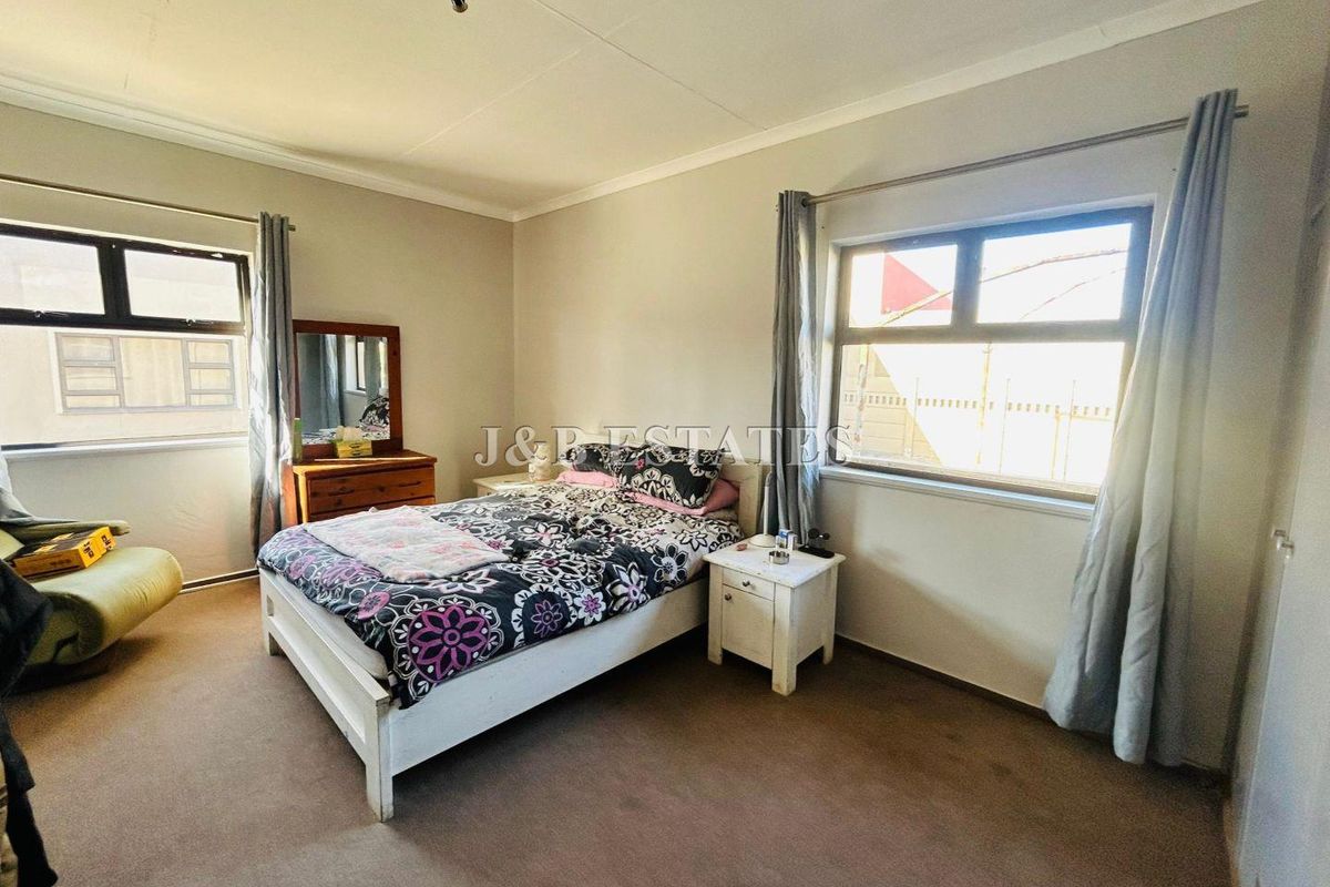 A functional bedroom featuring neutral wall tones, carpeted flooring, and dual windows providing natural light.