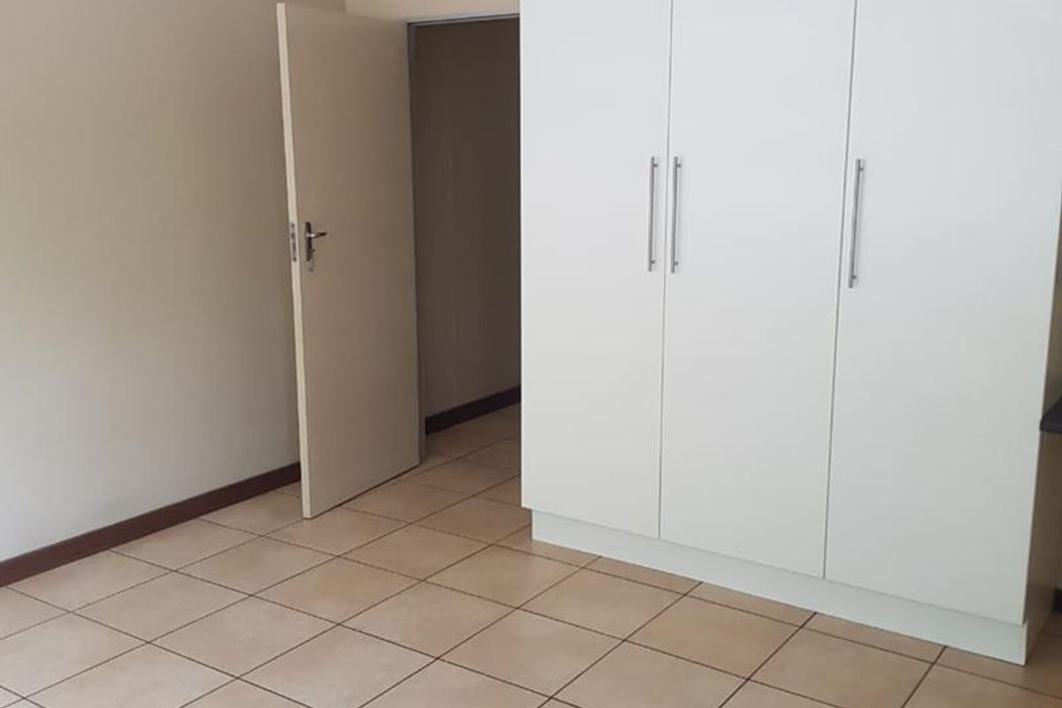 A bright, empty bedroom featuring neutral tiled flooring and built-in white cabinetry with modern handles.