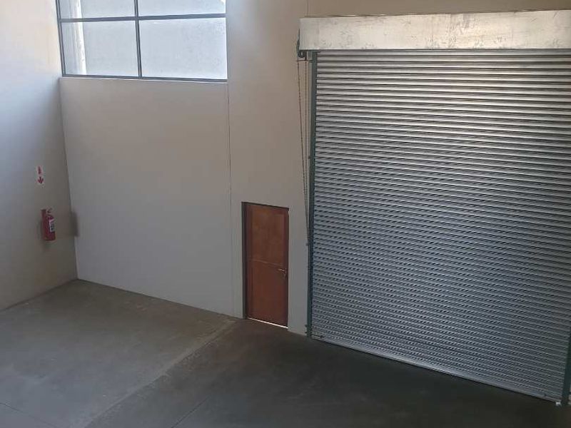 Spacious industrial utility area featuring high ceilings, concrete flooring, a large roller shutter door, and high-level windows for natural light.