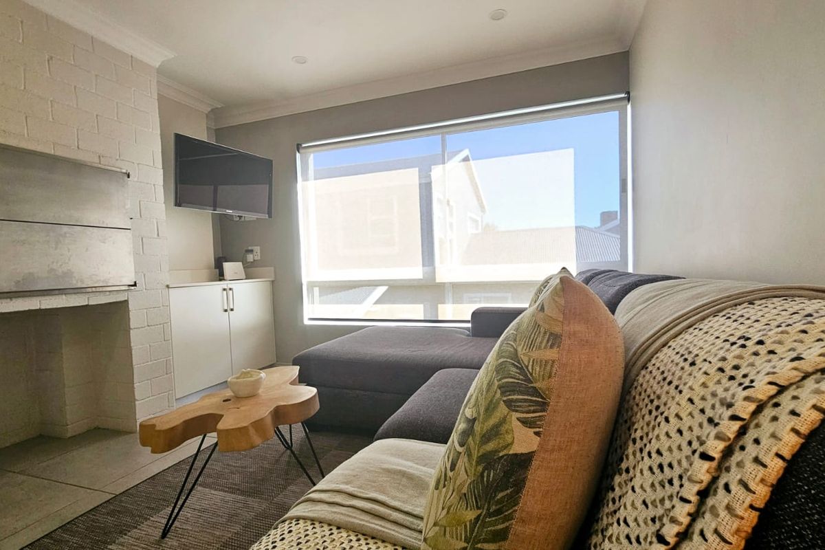A comfortable living room featuring a built-in fireplace, custom cabinetry, and large windows with roller blinds, offering a bright and functional space.