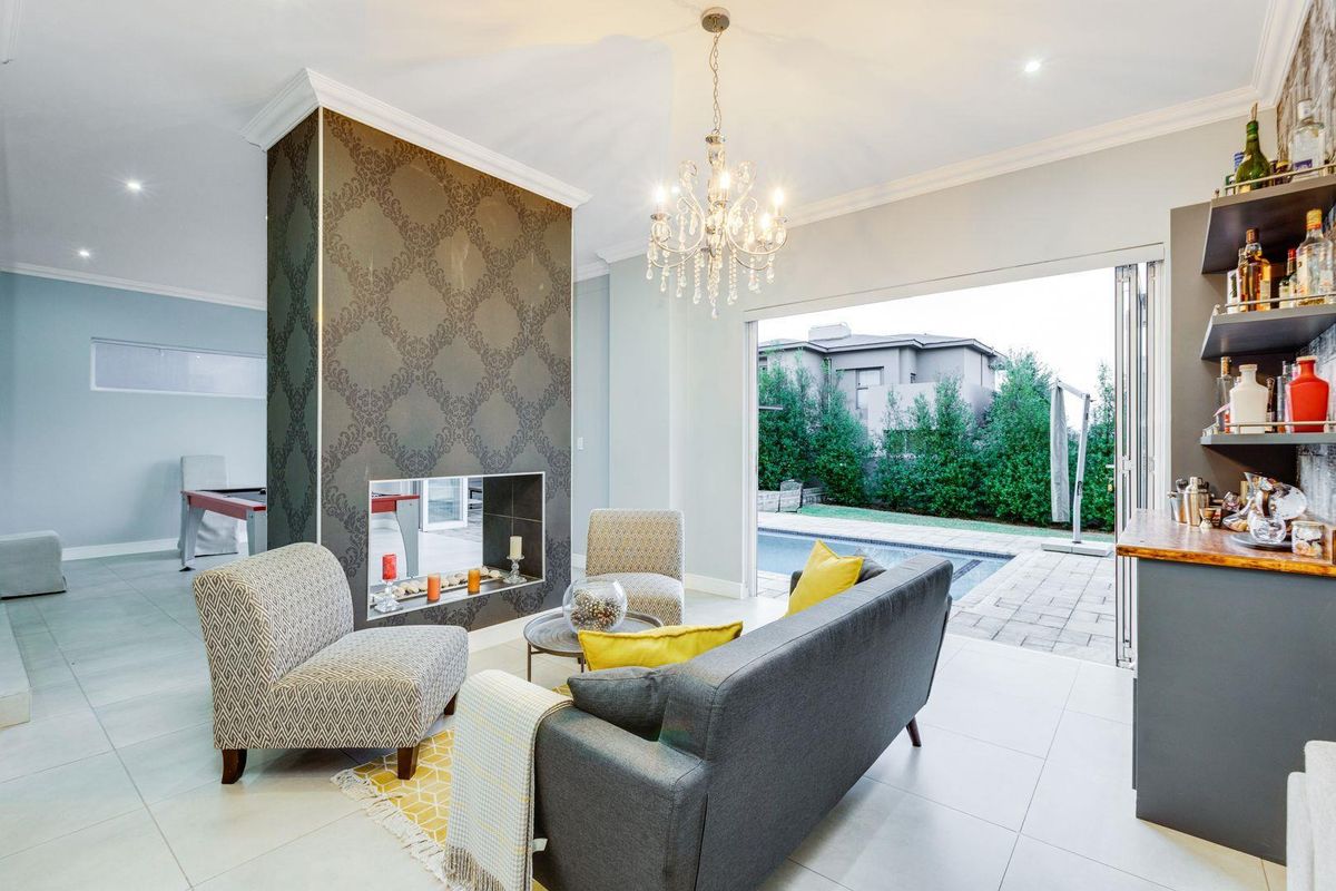 Spacious living area featuring a central double-sided fireplace, elegant chandelier, and large folding doors opening onto the patio and pool area.