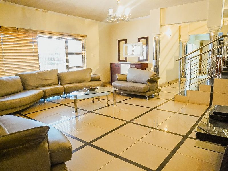 Spacious living room featuring large format tiled flooring, a modern stainless steel staircase railing, and decorative columns, with visible ceiling water staining.