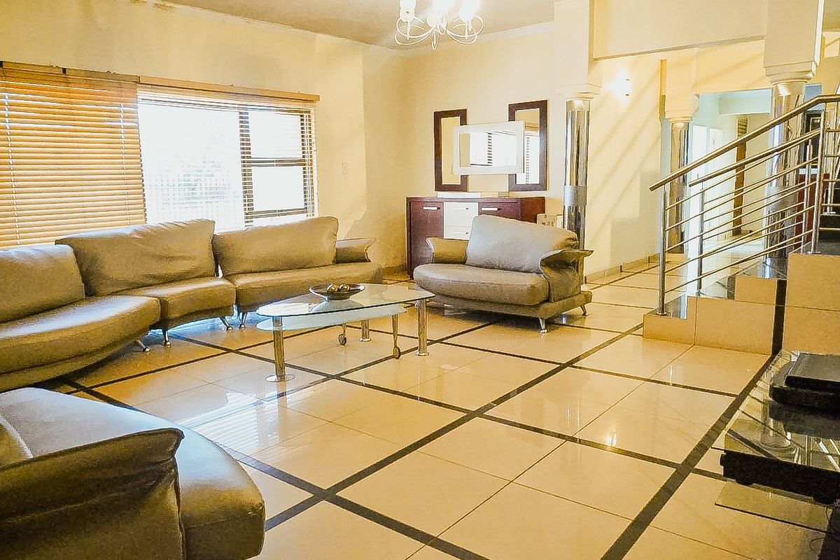 Spacious living room featuring large format tiled flooring, a modern stainless steel staircase railing, and decorative columns, with visible ceiling water staining.