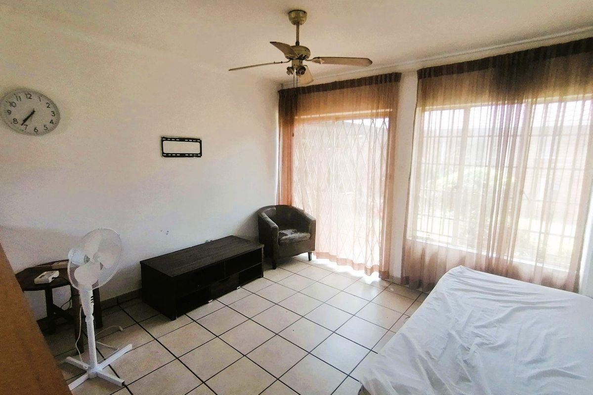 A bedroom featuring tiled flooring, a ceiling fan, and large windows with curtains, providing natural light and access to the exterior.