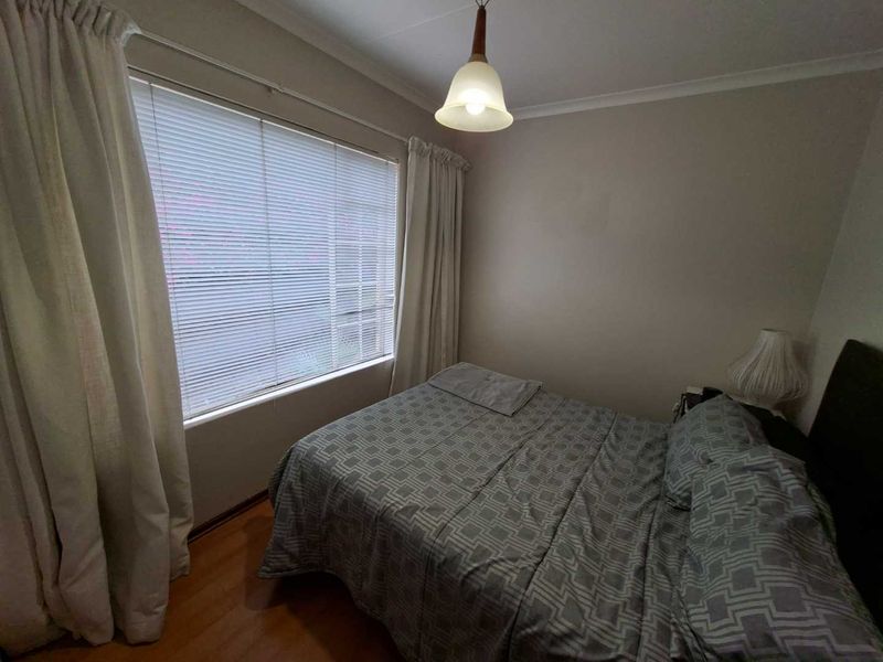 A standard bedroom featuring laminate flooring, venetian blinds, and neutral wall finishes, providing a functional and comfortable sleeping space.