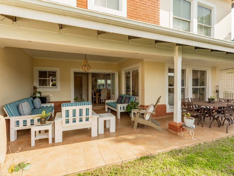A spacious covered patio featuring tiled flooring, brick accents, and direct access to the interior through sliding glass doors, overlooking the garden area.