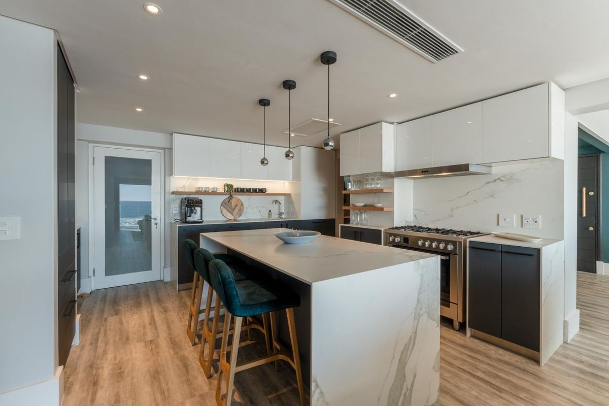 Modern kitchen featuring a large marble-topped island, sleek cabinetry, integrated gas range, and recessed ceiling lighting with a view of the ocean.