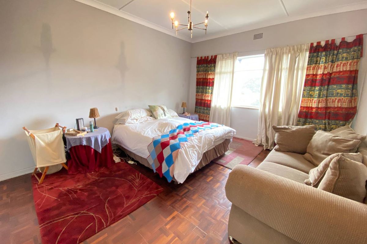 Spacious bedroom featuring classic parquet flooring, large windows with natural light, and a traditional ceiling light fixture.