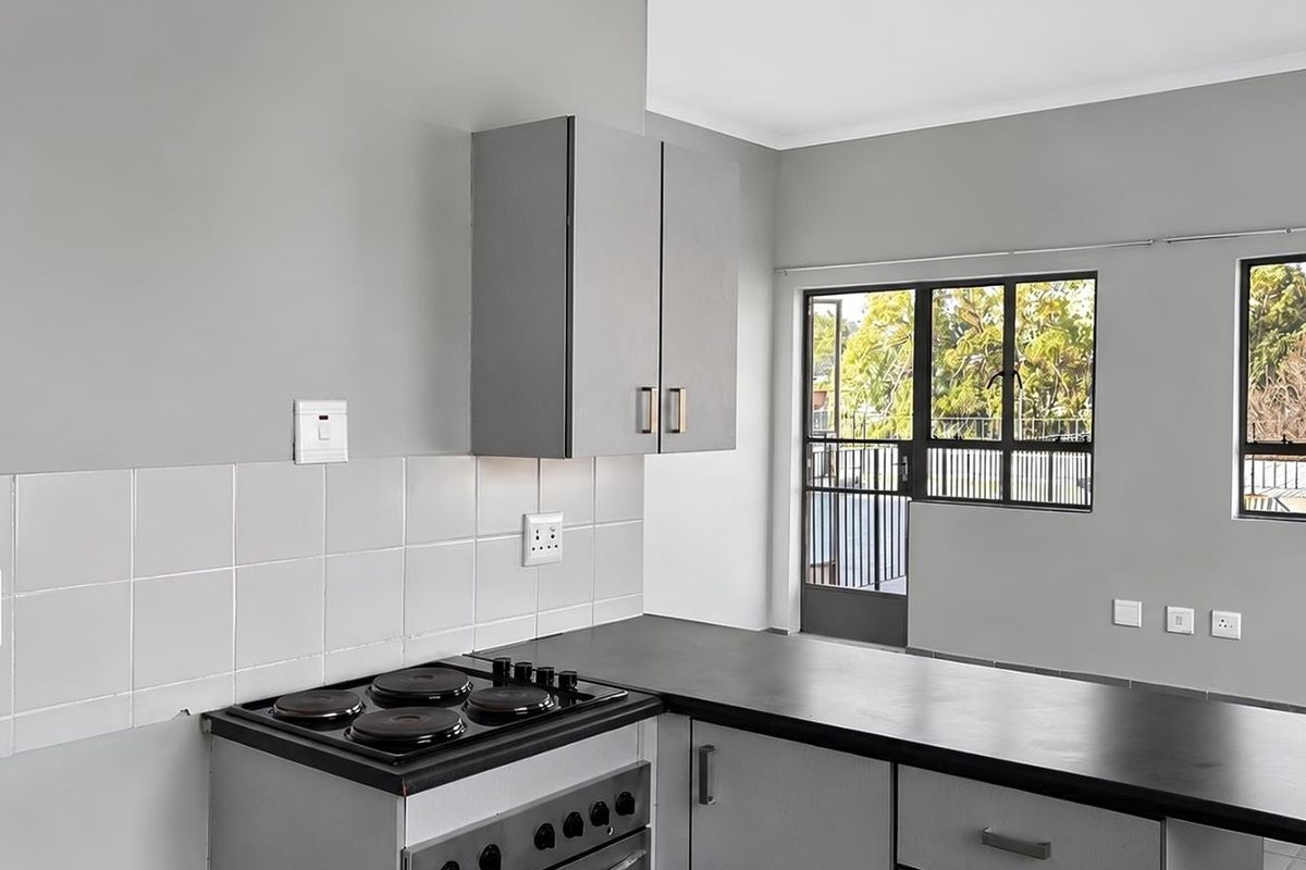 A clean, functional kitchen featuring grey cabinetry, dark countertops, a built-in stove, and a tiled backsplash with direct access to an outdoor area.