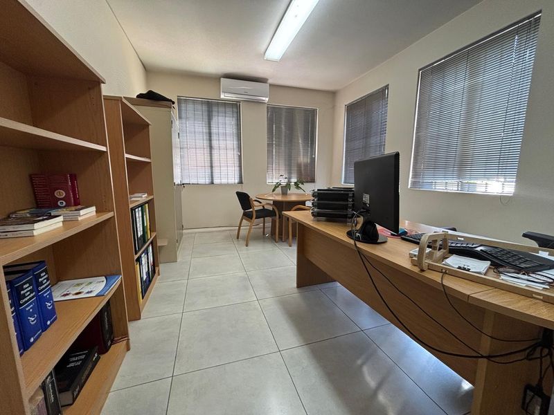 A functional office space featuring tiled flooring, venetian blinds, and a wall-mounted air conditioning unit, providing a practical work environment.
