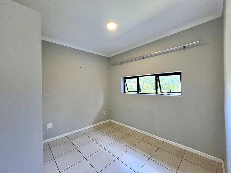 A clean, empty bedroom featuring neutral tiled flooring, a top-hung window with a curtain rod, and simple wall finishes.