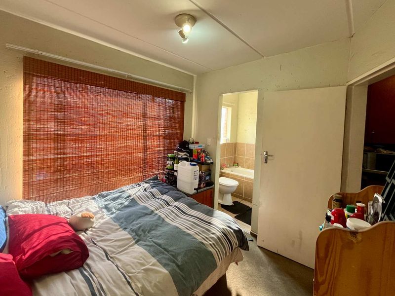 A bedroom featuring a window with a bamboo blind and an en-suite bathroom with a bathtub and toilet.