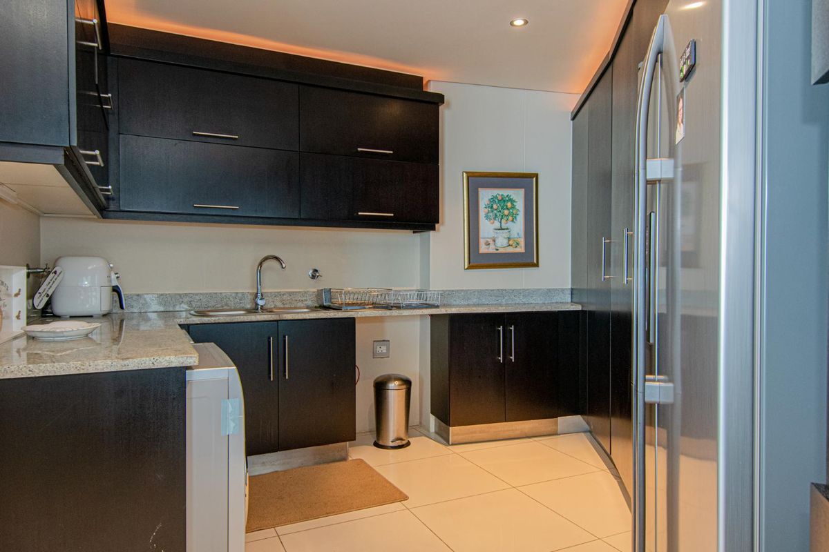 A modern kitchen featuring dark cabinetry, granite countertops, a stainless steel sink, and integrated storage solutions with tiled flooring.
