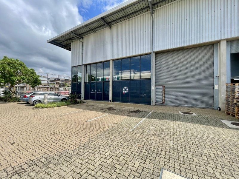 Front elevation of a mixed-use industrial unit featuring a large roller shutter door, expansive glass frontage, and dedicated paved parking area.