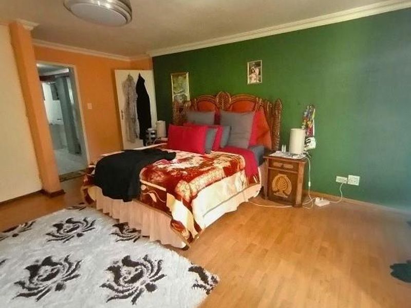 Spacious bedroom featuring laminate flooring and a green accent wall, with an adjoining doorway leading to an adjacent room.