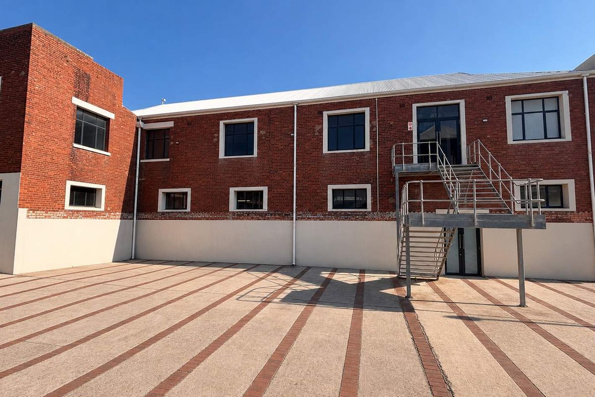 A view of the rear exterior of a brick office building featuring a paved courtyard and an external metal staircase providing access to the upper level.