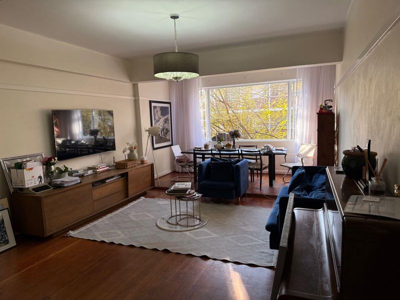 Spacious open-plan living and dining area featuring warm hardwood flooring, a large picture window with natural light, and a central pendant light fixture.