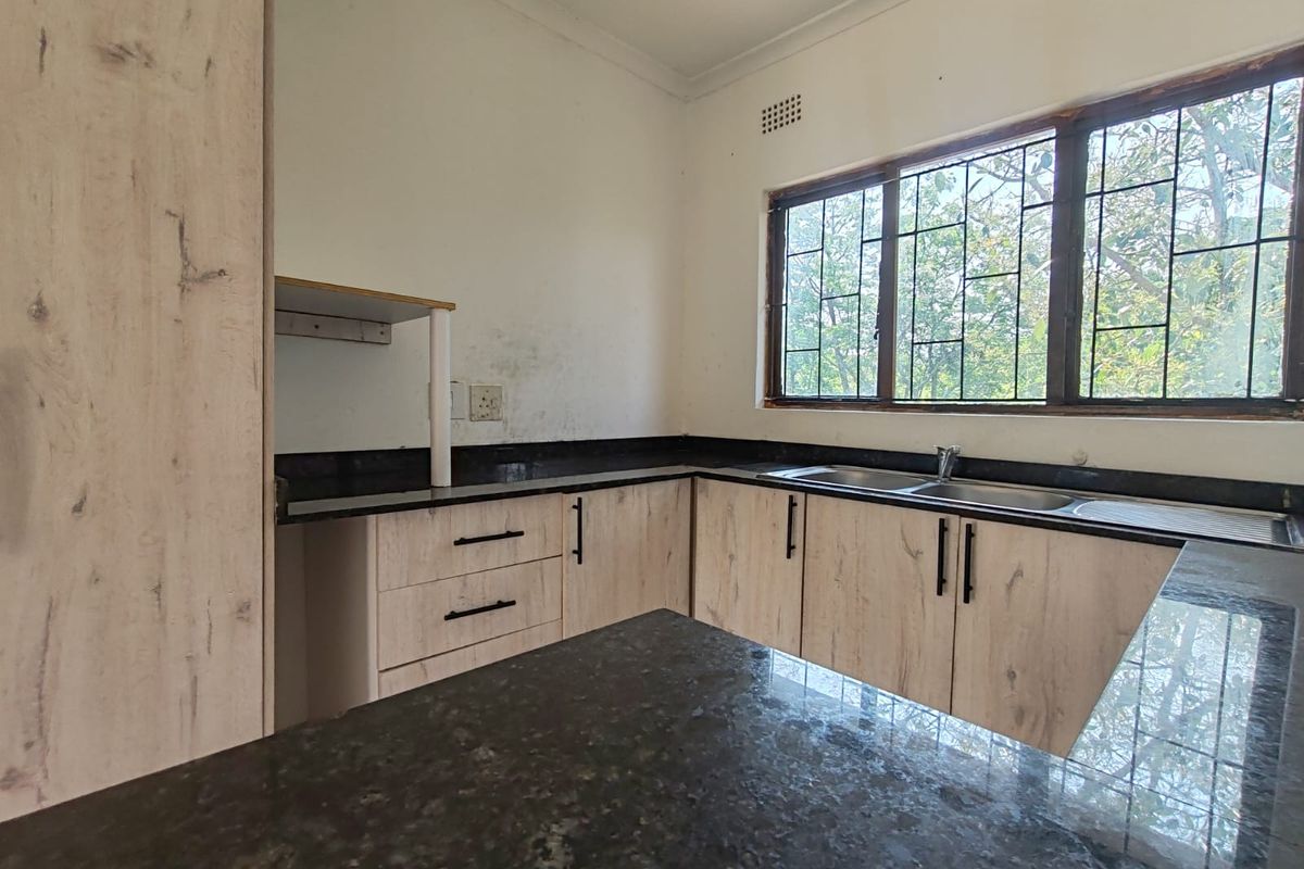 A functional kitchen featuring light wood-look cabinetry, dark granite countertops, and a double bowl sink, with large windows providing natural light.