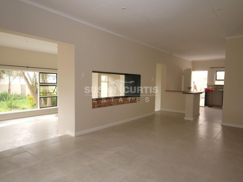 Spacious open-plan living area featuring neutral tiled flooring, a built-in breakfast bar, and an internal brick feature wall with recessed lighting.