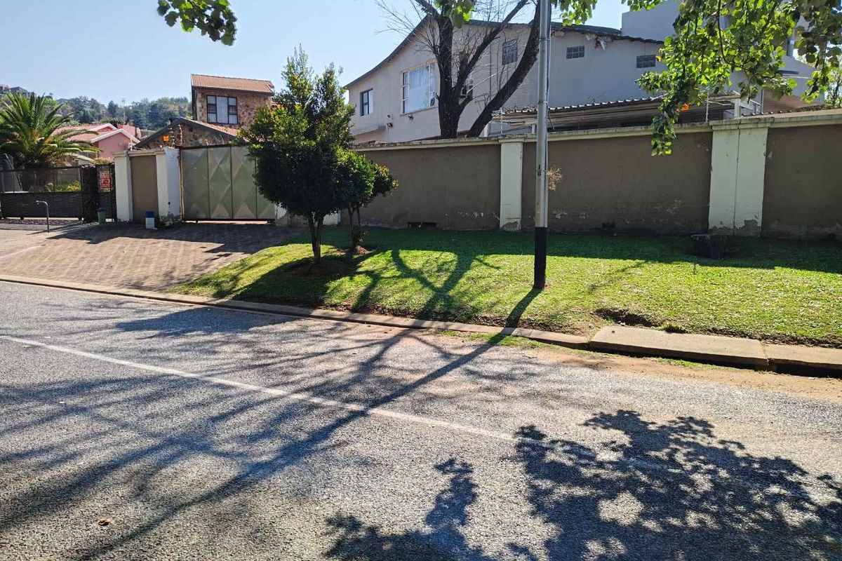 Street view of the property showing the perimeter wall, paved driveway entrance, and metal gate access.
