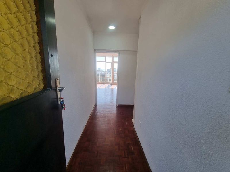 A bright entrance hallway featuring classic parquet flooring and a recessed downlight, leading directly into the main living area of the apartment.