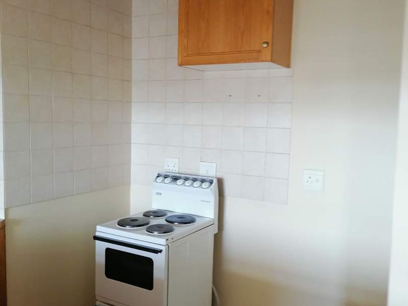 A compact kitchen area featuring a freestanding electric stove, wall-mounted wooden cabinetry, and tiled splashback finishes.