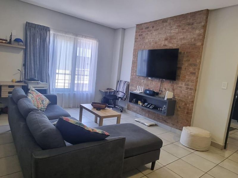 A comfortable living room featuring an exposed brick accent wall, built-in media shelving, and a dedicated workspace area with tiled flooring throughout.