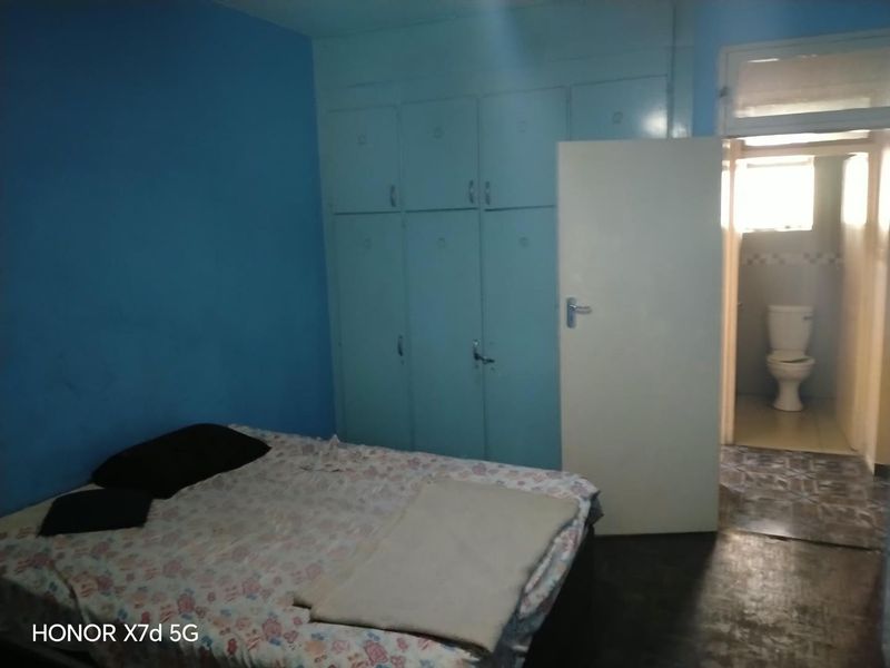 A bedroom featuring built-in cupboards and an attached en-suite bathroom with a toilet, requiring cosmetic updates to improve the overall aesthetic.