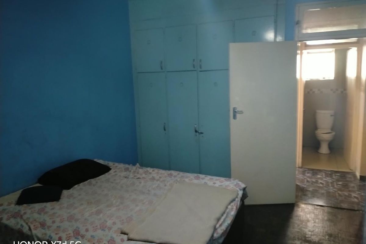 A bedroom featuring built-in cupboards and an attached en-suite bathroom with a toilet, requiring cosmetic updates to improve the overall aesthetic.