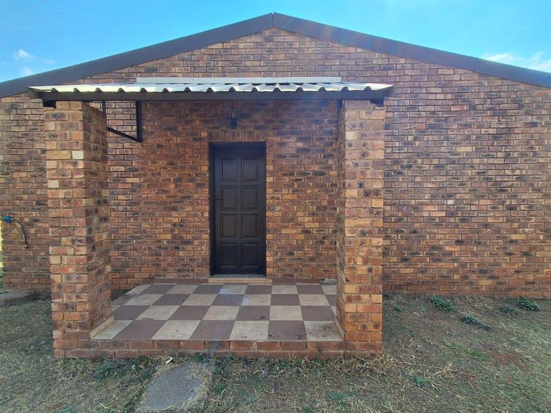 Front entrance of a face brick house featuring a covered porch with tiled flooring and brick support pillars.