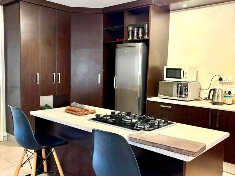 Modern kitchen featuring dark wood cabinetry, a central island with a built-in gas hob, and stone countertops, providing a functional and stylish cooking space.
