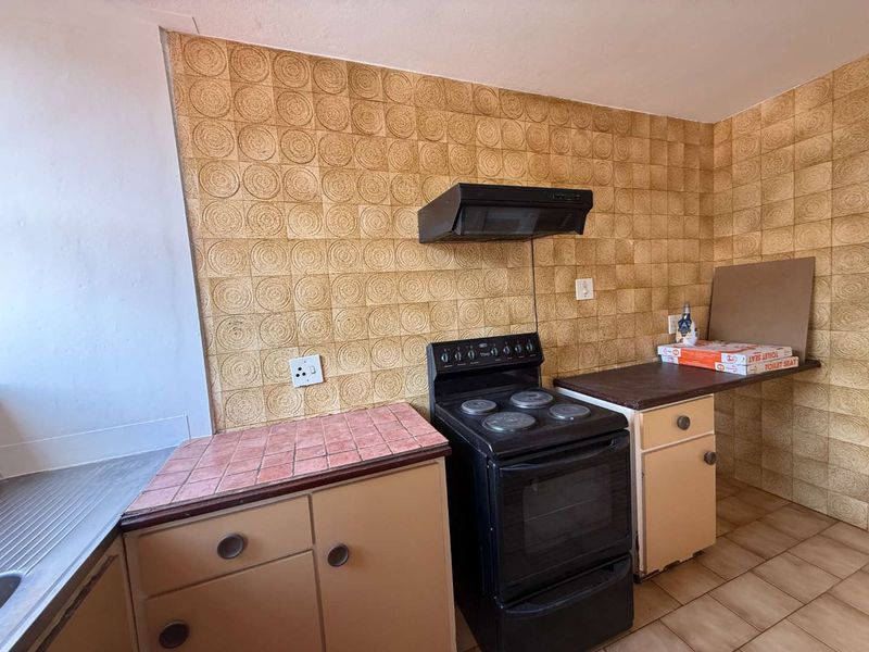 A dated kitchen featuring original cabinetry, tiled countertops, and a built-in electric stove with an extractor fan.