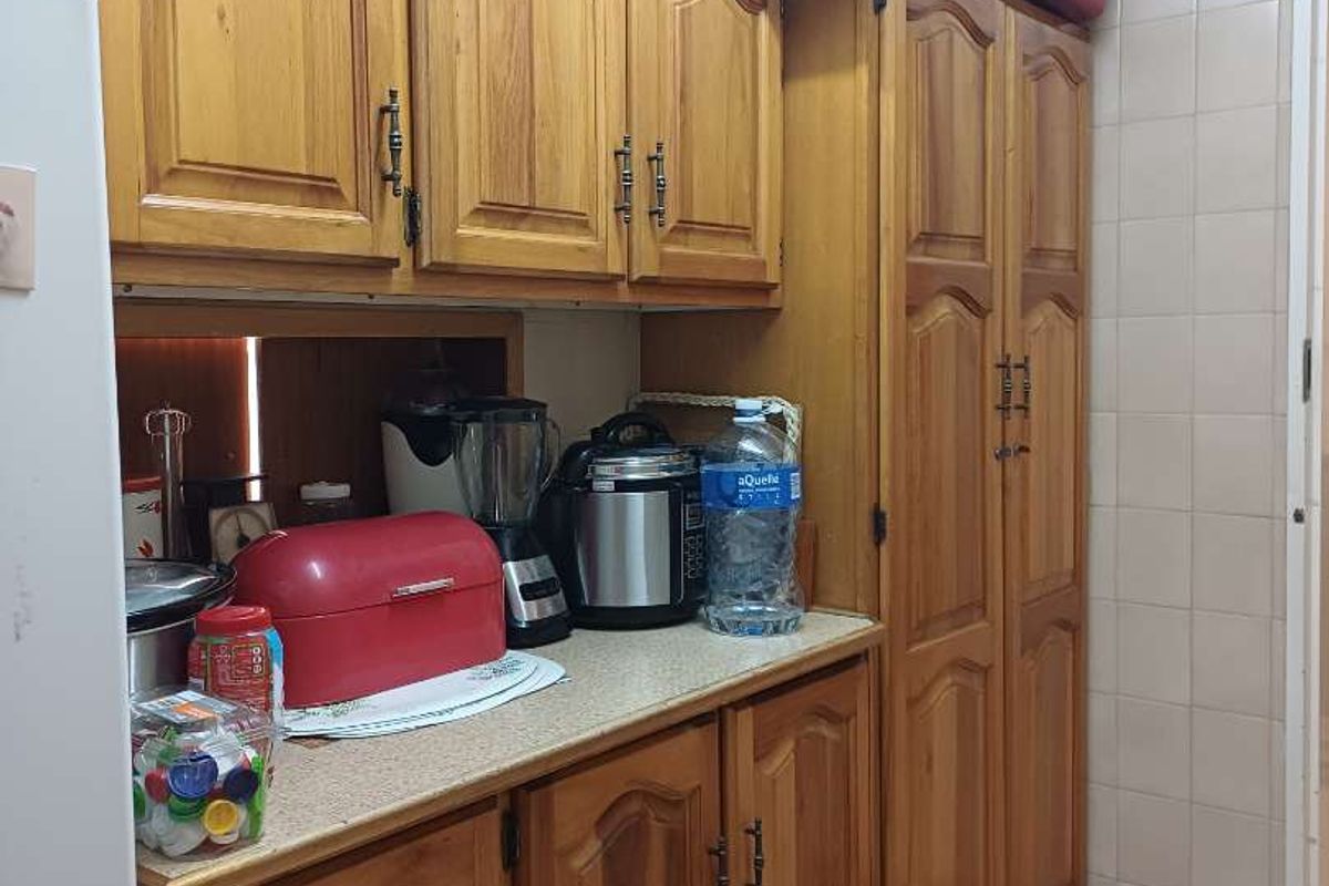 A functional kitchen area featuring traditional timber cabinetry, laminate countertops, and tiled flooring, providing ample storage space.