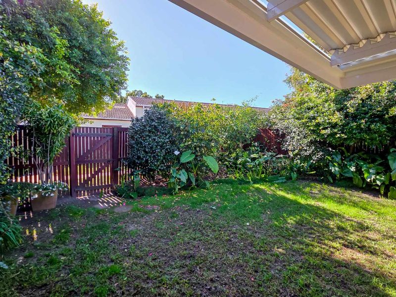 A covered patio area overlooking a private garden with a timber fence and gate.